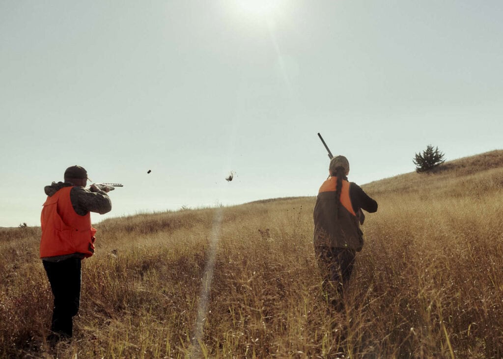 Two hunters aiming rifles in a grassy field during daytime in Nebraska.