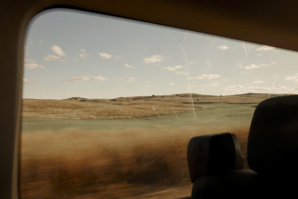 View of a golf course through a car window with a clear sky.